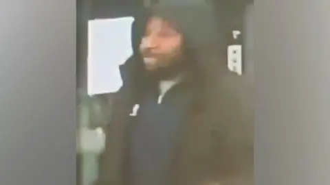 CCTV A blurry CCTV image of Anthony Williams wearing a hooded black coat and a blue zip sweater . he has a beard and moustache.