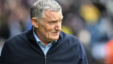 Tony Mowbray wearing a blue cardigan looks to his left