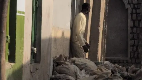 A man standing in front of a home with several bags in front of the house