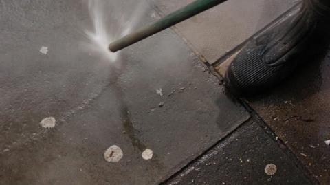 Council worker uses an Aqua Fortis or 'Gumbuster' which are now being used by councils across the country in a bid to remove chewing gum from roads. A black rubber boot can also be seen in the image
