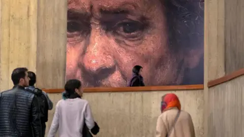 Morteza Nikoubazl/Getty Images Young Iranian people walk under a copy of a detail of a self-portrait by Rembrandt (1659), the Dutch painter and printmaker, while visiting the ''Eye to Eye, Portraiture in Modern and Contemporary Art'' exhibition