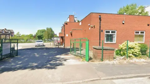 Google The gated entrance to a red-brick social club building on a sunny day.