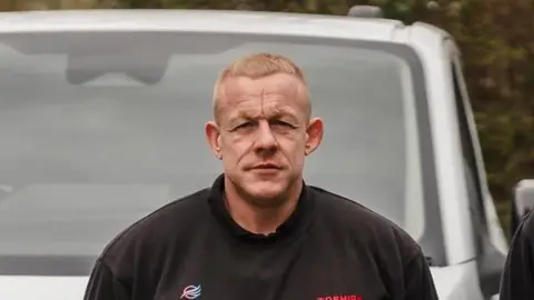 Cambridge Air Conditioning A man looking straight at the camera, wearing a black sweatshirt while standing in front of a white van.