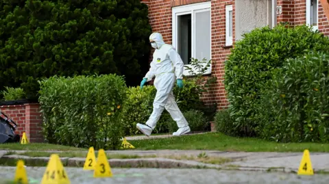 A man in a white hazmat suit walks out of a house in Stade, Germany.