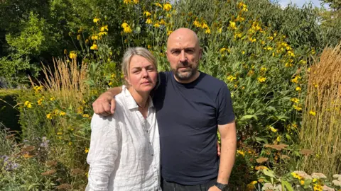 A man and woman embrace. They look concerned. 