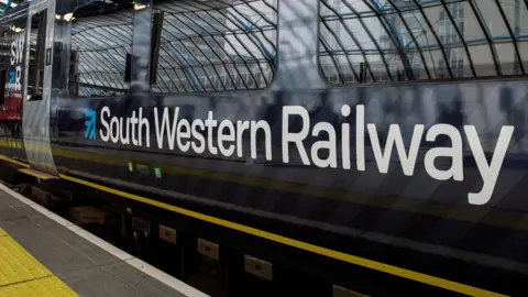 Bloomberg via Getty Images A file image showing the white and blue South Western Railway logo on a train with a yellow and light and dark blue livery as it is pulled into the platform