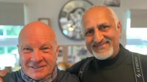Two men in grey tops, one with a bald head and the other with short white hair and a beard