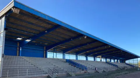 A blue and white grandstand with silver steps and railing and a blue roof