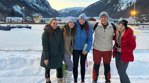 Kade Alford A picture of Maria and her four friends on a trip to Norway earlier this year. They are standing in the snow with snowy mountains behind them. Maria is second to the left and she has her arms wrapped around her friends' shoulders. The picture looks like it's been taken during a sunset. 