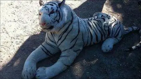 A large stuffed tiger toy. It is white with black stripes and in a prone position.
