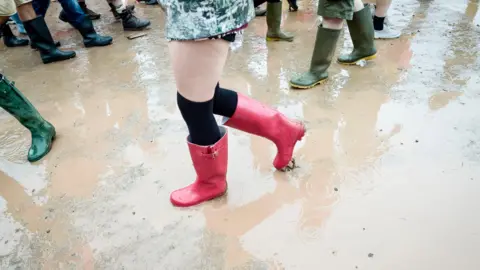 PA A picture shows someone wearing bright red wellies walking through a muddy puddle at the festival. 