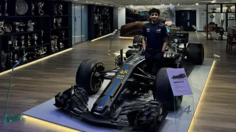 Otis Lawrence Otis Lawrence stood next to a 2018 F1 car wrapped in the esports team design. There is a trophy cabinet on the left showing the silverware from the teams wins.