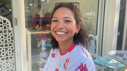 A woman in a football top sits outside a restaurant