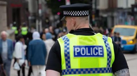 The back of the head of a policeman in uniform on patrol in a city, blurred out people are seen in front of him