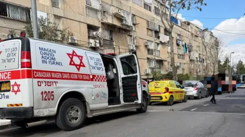 Magen David Adom ambulance and other vehicles on a street in north-west Jerusalem, near a daycare centre where two babies died (19 January 2026)
