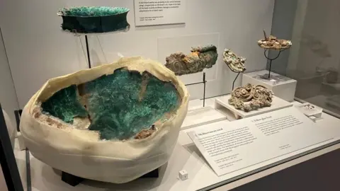 BBC/Joanita Musisi A large broken bowl wrapped in plaster. The inside of the bowl is blue. It is in a glass display case along with other metal objects.