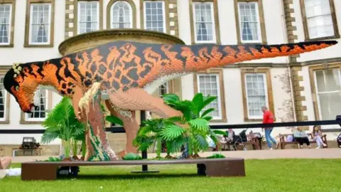 East Riding of Yorkshire Council A large brick model of a dinosaur. It is long and is orange and black. 