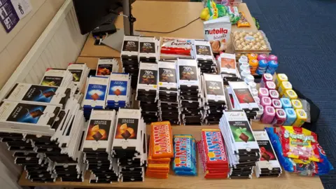 Hundreds of different brands of chocolates and sweets are stacked on top of each other on a wooden table.