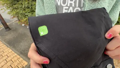 A close-up of a black pair of trousers. There is a green square sticker on them.
