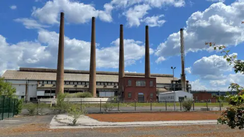 BBC/Spencer Stokes A factory with five large chimneys on a sunny day.