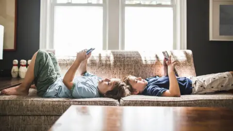 Getty Images Dois irmãos olhando para seus telefones. Foto posada por modelos