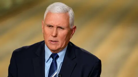 Mike Pence, with short grey hair, looks serious while wearing a navy suit jacket and tie 