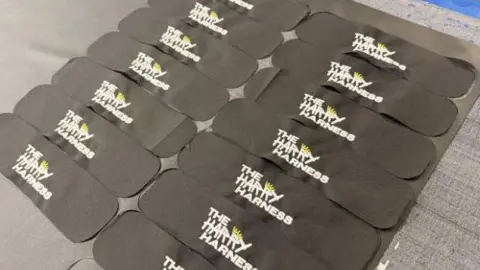 There are two rows of the Harry Harness, which has a black pad, positioned on a table in a warehouse. 