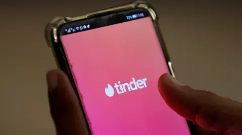 Reuters Close up of a person's hands holding a smartphone with the Tinder logo in white text on a pink background filling the screen