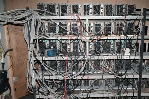 A series of machines being used to mine cryptocurrency. A series of wires are protruding from the machines.