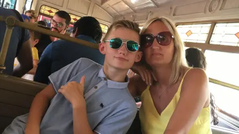 A woman in a yellow top sat next to a boy in a blue polo shirt, they appear to be in a restaurant.