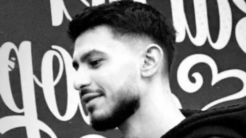 Sussex Police A black and white image of the side profile of a young man with short black hair and a black beard