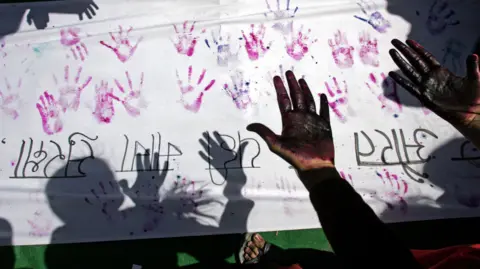 Getty Images A file photo of An Indian woman looking at her hands after making a hand impression on a banner during a street march against sexual harassment and marital violence to mark International Women's Day in New Delhi