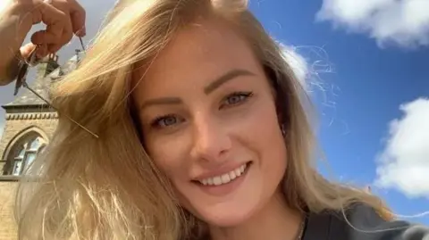Jade Damarell is smiling at the camera. She has long blonde hair and is holding a pair of sungalsses.