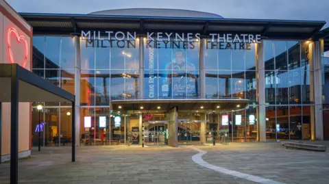 Getty Images Il Milton Keynes Theatre con la facciata in vetro visto dall'esterno al crepuscolo.