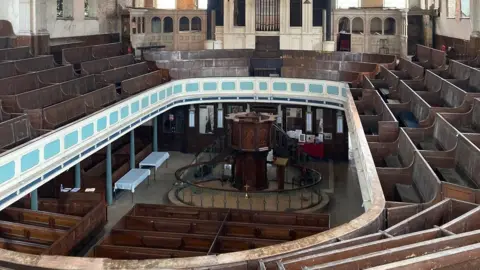 Re-Form Heritage The interior of a Victorian Methodist chapel. There is a circular balcony with raked seating. In the middle of the building is a pulpit with steps either side leading up to it. There is a pipe organ in the centre of the image.