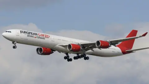 European Cargo A European Cargo plane in flight, with its white body, red tail fin and red engines.