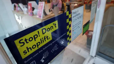 A sign warning not to shoplift attached to a glass door at a Boots.