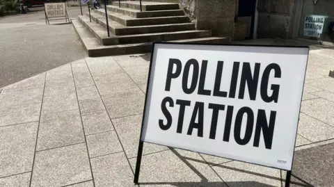A metal sign on a stand saying "Polling Station" on a small plaza next to some grey stone steps.