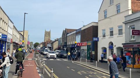 A wide shot of Keynsham high street showing pedestrians and cyclists on either side