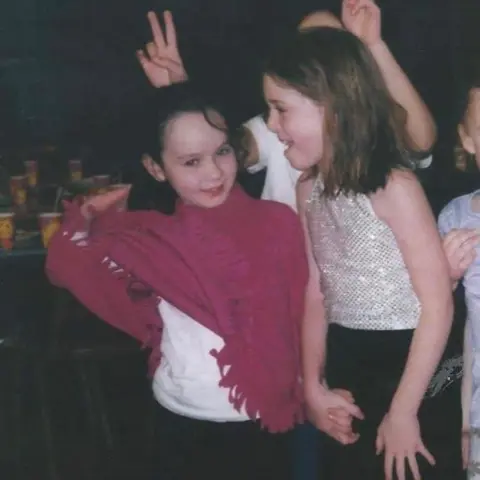 Harriet Barnsley A photo of two young girls at a party. The girl on the left wears a pink poncho and the girl on the right wears a sequin top.