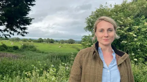 Conservative party Meg Powell-Chandler stood in tweed brown jacket in a field