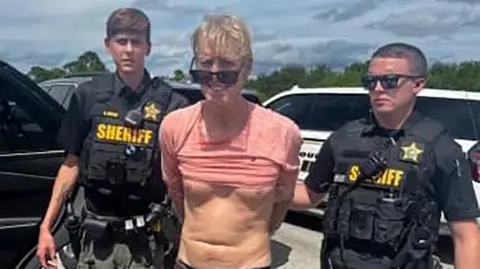 Reuters / Martin County Sheriff's Office A inactive  from a constabulary  video showing Ryan Routh, a antheral   with a mop of blond hair, sunglasses and a pinkish  T-shirt pulled up   implicit    his stomach, flanked by 2  deputies from the Martin County Sheriff's Office