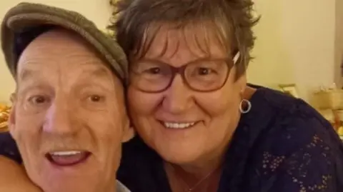 West Mercia Police A woman with short hair and glasses has her arms round the shoulders of her husband. He is wearing a flat cap and had a light moustache. The pair are smiling and look jolly.