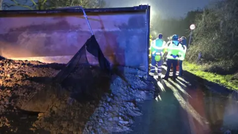 Bedford Borough Council Part of a lorry can be seen with blurred images of poeple in hi-vis jackets standing next to it on the road
