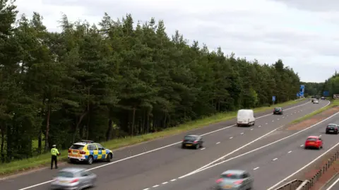 PA Media A police car sits near Junction 9 of the M9 after the car was found