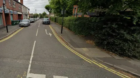 Generic image of Villa Road, with cars on both sides of the street. There are trees and bushes to the right of the road on the photo, approaching the junction in the foreground.