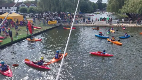 Bedford Borough Council Loads of people on water, taking part in sporting activities. There are trees in the distance, and a few buildings. There are mostly canoes on the water. 
