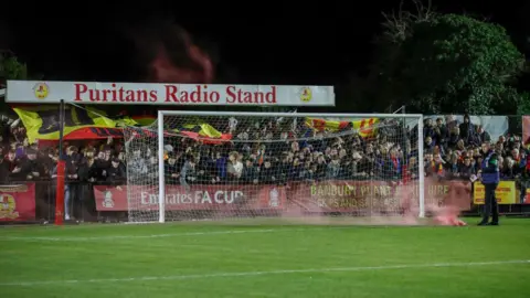 Flares are thrown onto the field of play during the Emirates FA Cup First Round match between Banbury United and Barrow at Spencer Stadium.