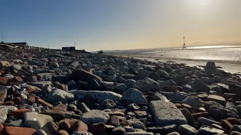 A view over 'Blitz Beach' showing piles of stone, bricks and ceramic on a beach at sunset
