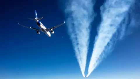 Airbus An Airbus A350 flies behind the condensation trails of another jet fighter in the blue sky